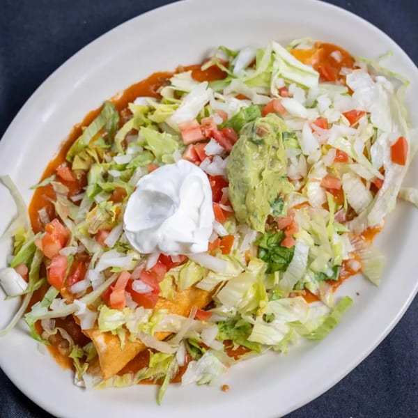 Enchiladas covered in red sauce, lettuce, diced tomatoes, onions, guacamole, and sour cream.
