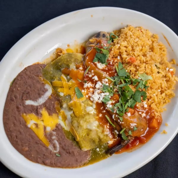 A white plate with enchiladas, refried beans, and Mexican rice, garnished with cheese and cilantro.
