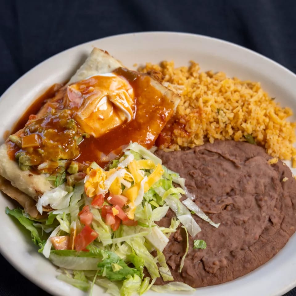 A plate of Mexican food with a burrito, rice, refried beans, and a side salad.