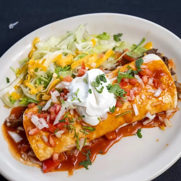 A large burrito covered in red sauce, sour cream, pico de gallo, and cilantro, with a side salad.