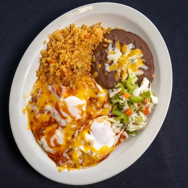 Huevos Rancheros with rice, refried beans, and a side salad on a white oval plate.