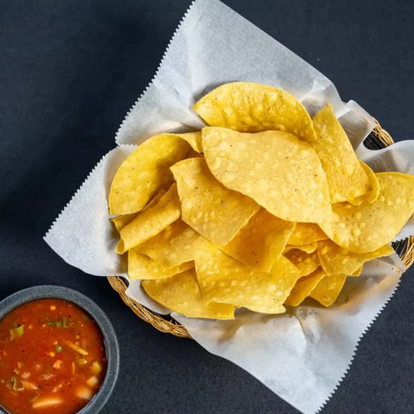 A basket of golden tortilla chips with a side of vibrant red salsa on a dark surface.